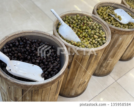 Barrels of green and black olives with scoops in wooden containers in a market setting Barrels of green and black olives with scoops in wooden containers in a market setting 135958584