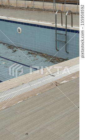 Empty swimming pool with blue tiles and metal ladder in outdoor area, suitable as background 135958592