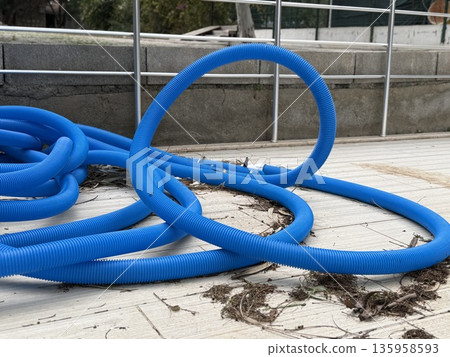 Blue pool hose coiled on wooden deck with leaves and metal railing background Blue pool hose coiled on wooden deck with leaves and metal railing background 135958593