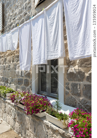 Vertical street photography with a sunlit stone house features white laundry Vertical street photography with a sunlit stone house features white laundry 135959014
