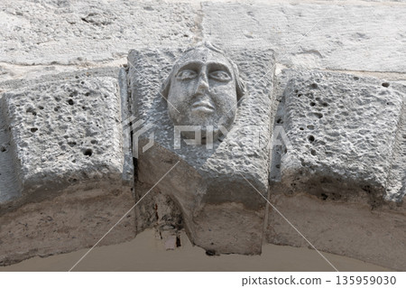 A weathered stone arch features a carved human face A weathered stone arch features a carved human face 135959030