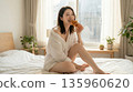 清晨的陽光灑在床上，一位年輕的日本女子正躺在床上吃著牛角麵包。 135960620