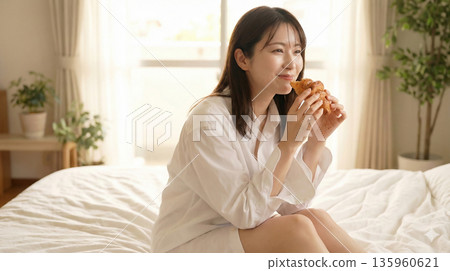 一位神態放鬆的女士在床上享用早餐，臉上洋溢著笑容。 135960621