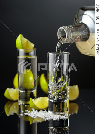 Tequila shots with salt and lime slices on a black reflective background. 135960647
