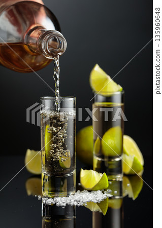 Tequila shots with salt and lime slices on a black reflective background. Tequila shots with salt and lime slices on a black reflective background. 135960648