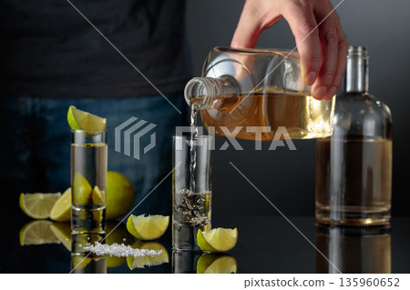 Tequila shots with salt and lime slices on a black reflective background. 135960652