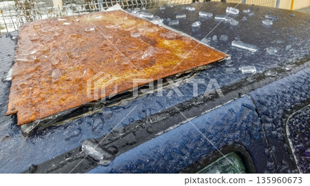 Rusted metal panel tilted on frozen car roof with melting ice and frost crystals reflecting cold winter conditions and textured corrosion over dull surface. Rusted metal panel tilted on frozen car roof with melting ice and frost crystals reflecting cold winter conditions and textured corrosion over dull surface. 135960673