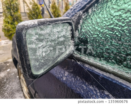 Car mirror and side window covered in frozen condensation and ice crystals, highlighting thick winter buildup and reduced visibility on snowy day. Car mirror and side window covered in frozen condensation and ice crystals, highlighting thick winter buildup and reduced visibility on snowy day. 135960676