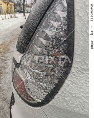 Close-up of rear car taillight covered in ice, showing frosted surface, frozen water droplets, and slippery glaze reflecting wintertime road conditions. Close-up of rear car taillight covered in ice, showing frosted surface, frozen water droplets, and slippery glaze reflecting wintertime road conditions. 135960696