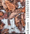 Top-down view of bark mulch and snow on garden soil, emphasizing rough woody textures blending with frozen granular ice and seasonal melting patterns. 135960749