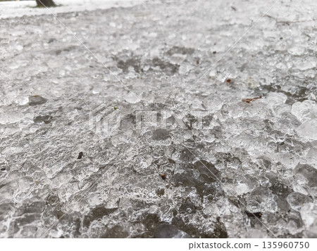 Surface of compacted ice and snow showing uneven frozen texture with granular frost particles covering the ground during a cold winter season outdoors. Surface of compacted ice and snow showing uneven frozen texture with granular frost particles covering the ground during a cold winter season outdoors. 135960750