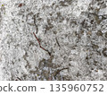 Close-up of ice and soil mixture showing cracks and embedded twigs within rough frozen surface, reflecting harsh winter outdoor ground conditions. 135960752
