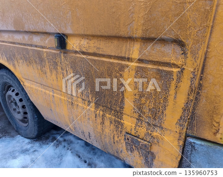 Dirty yellow van with road grime streaks parked on snowy surface, showing contrast between muddy residue and bright paint during winter weather conditions. 135960753