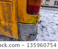 Rear corner of yellow vehicle heavily stained with greenish grime and snow residue, showcasing age, neglect, and weather exposure during winter. 135960754