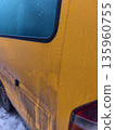 Side view of yellow van with icy windows and dirty panels, highlighting frozen condensation, grime accumulation, and wintertime weather conditions. 135960755