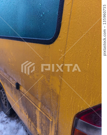Side view of yellow van with icy windows and dirty panels, highlighting frozen condensation, grime accumulation, and wintertime weather conditions. 135960755