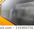 Frozen condensation completely covering yellow van window, creating textured icy surface and blurred view of interior objects through thick winter frost. 135960756