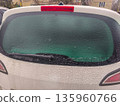 Frozen rear windshield of white vehicle with greenish tint and complete ice coverage, creating opaque appearance due to heavy winter frost layer. 135960766