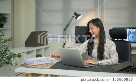 Businesswoman using laptop computer and picking a document paper in office Businesswoman using laptop computer and picking a document paper in office 135960957