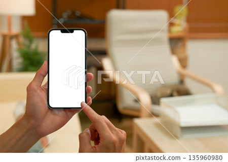 Close up view of a man using blank screen smartphone at living room Close up view of a man using blank screen smartphone at living room 135960980