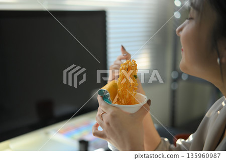 Closeup young woman eating instant noodles in office workplace Closeup young woman eating instant noodles in office workplace 135960987