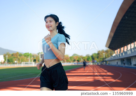 Young Asian woman jogging on outdoor running track in morning sunlight 135960999