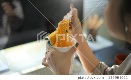 Closeup young woman eating instant noodles in office workplace Closeup young woman eating instant noodles in office workplace 135961021