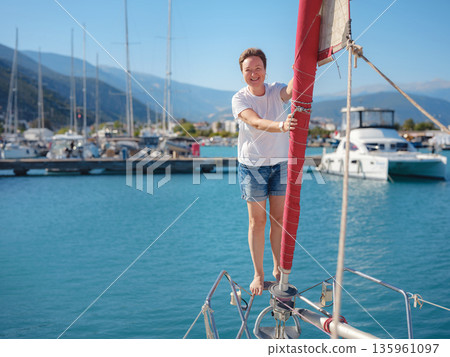 Female sailor holds white sail cloth preparing to hoist sails on yacht. Physical activity and boat handling skills are shown during preparation for sailing trip near Finike coast. 135961097