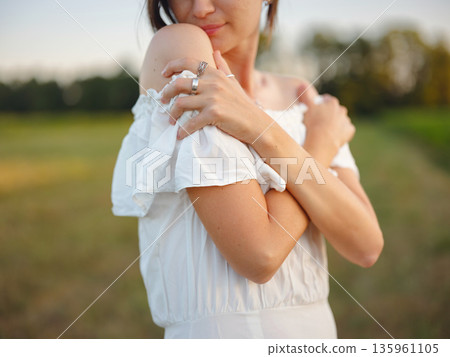 Beautiful woman in white dress standing in summer field during golden sunset in Croatia, warm sunlight, romantic evening mood, natural countryside atmosphere, soft wind and peaceful scene Beautiful woman in white dress standing in summer field during golden sunset in Croatia, warm sunlight, romantic evening mood, natural countryside atmosphere, soft wind and peaceful scene 135961105
