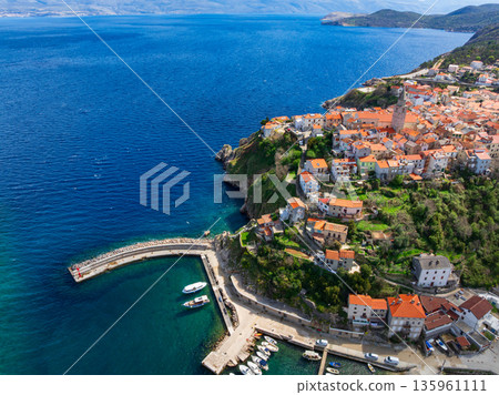 Drone captures stunning top view of Vrbnik towns on Krk Island in Croatia. Blue Adriatic Sea meets rocky coastline and traditional Mediterranean architecture from above. 135961111