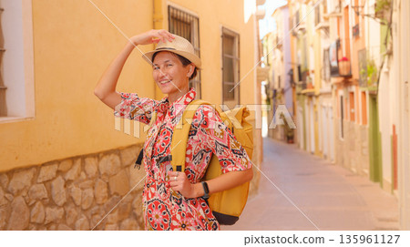 Woman in dress strolls through colorful streets of Spanish coastal town of La Vila Joiosa or Villajoyosa. sunny winter atmosphere highlights charm of Mediterranean architecture and quiet seaside life 135961127