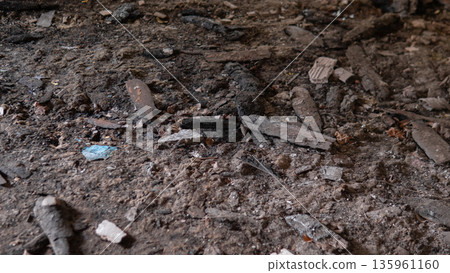 Dirt and debris cover an old wooden floor in a dimly lit room. Broken wood pieces and other waste are scattered, showing signs of neglect and decay in the space. 135961160