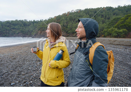 Couple enjoys Turkish coastline. Sitting on stones, watching sea waves, relaxing together, slow romantic moment near calm blue water under soft winter light. Couple enjoys Turkish coastline. Sitting on stones, watching sea waves, relaxing together, slow romantic moment near calm blue water under soft winter light. 135961178