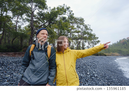 Couple enjoys Turkish coastline. Sitting on stones, watching sea waves, relaxing together, slow romantic moment near calm blue water under soft winter light. 135961185