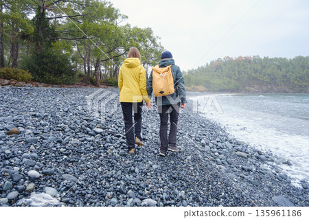 Couple enjoys Turkish coastline. Sitting on stones, watching sea waves, relaxing together, slow romantic moment near calm blue water under soft winter light. Couple enjoys Turkish coastline. Sitting on stones, watching sea waves, relaxing together, slow romantic moment near calm blue water under soft winter light. 135961186