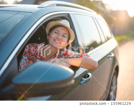 Traveler woman in red ethnic dress and hat drives car through scenic countryside of Croatia in summer. Surrounded by lush fields and forests, she enjoys peaceful and adventurous road trip 135961229