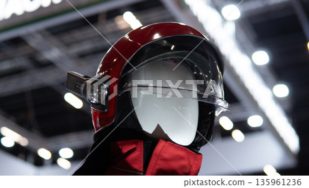 Mannequin wearing red helmet front closeup showing visor mechanism and gear texture under exhibition lights with glossy finish and product display atmosphere for safety marketing Mannequin wearing red helmet front closeup showing visor mechanism and gear texture under exhibition lights with glossy finish and product display atmosphere for safety marketing 135961236