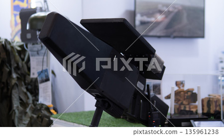 compact drone countermeasure launcher on display, rugged matte finish mounted on adjustable tripod, closeup of sensor array and optical housing, exhibition booth lighting, designed compact drone countermeasure launcher on display, rugged matte finish mounted on adjustable tripod, closeup of sensor array and optical housing, exhibition booth lighting, designed 135961238