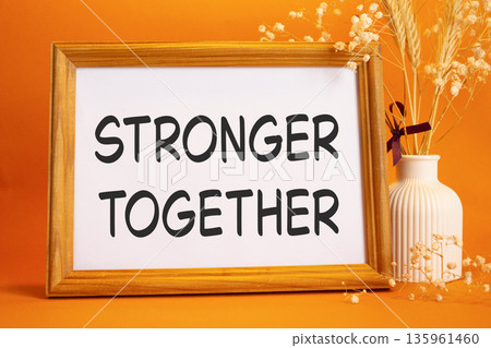 Stronger together symbol. Concept words Stronger together on beautiful wooden picture frame. Beautiful orange background with flower vase. Business and Stronger together concept. Copy space. Stronger together symbol. Concept words Stronger together on beautiful wooden picture frame. Beautiful orange background with flower vase. Business and Stronger together concept. Copy space. 135961460