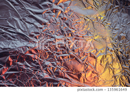 Crumpled aluminum foil texture creating an abstract background with colorful light reflections Crumpled aluminum foil texture creating an abstract background with colorful light reflections 135961649