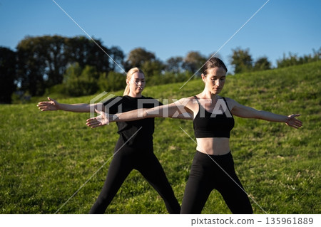Women practicing yoga outdoors in a serene park during daytime sunlight 135961889