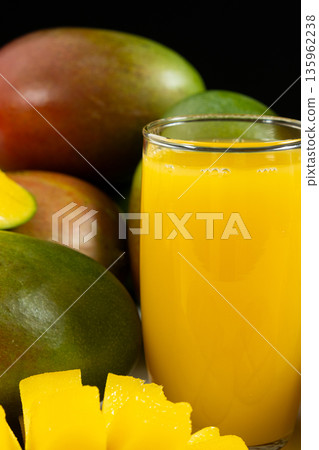 Glass of fresh mango juice surrounded by whole and sliced fruits. 135962238