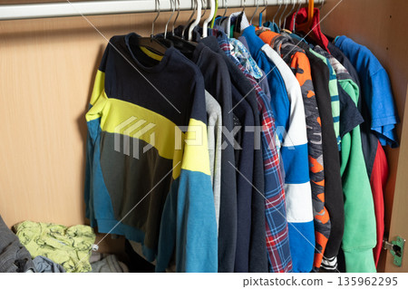 Organization of space in the wardrobe for childrens clothes, hanging sweaters on hangers in a wooden wardrobe Organization of space in the wardrobe for childrens clothes, hanging sweaters on hangers in a wooden wardrobe 135962295