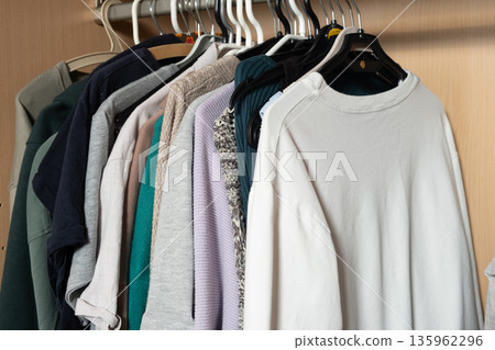 Minimalist knitwear and shirt organization on hangers in bright closet Minimalist knitwear and shirt organization on hangers in bright closet 135962296