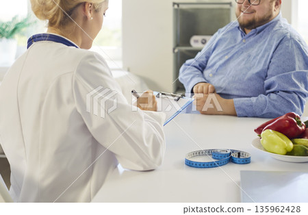 Nutritionist consulting overweight patient with vegetables, tape measure in clinic 135962428