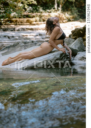 Attractive slim woman in bikini posing on rock river. Attractive slim woman in bikini posing on rock river. 135962948
