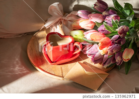 Heart Shaped Coffee Cup with Tulips and Envelope on Bed. Romantic Valentines Day Celebration Heart Shaped Coffee Cup with Tulips and Envelope on Bed. Romantic Valentines Day Celebration 135962971