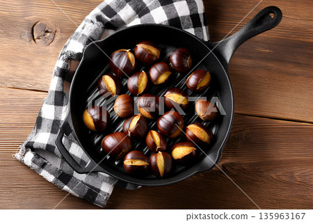 Roasted chestnuts in a cast iron skillet on a wooden table with checkered cloth 135963167