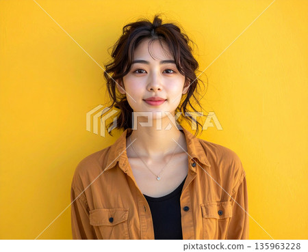 一位面帶微笑的女子站在一面明亮的黃色牆前。 一位面帶微笑的女子站在一面明亮的黃色牆前。 135963228