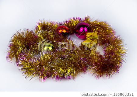 Tangle of sparkly gold tinsel with pink accents frames Christmas balls and small gold gift boxes on white background. These festive decorations set bright, holiday scene. Soft focus New Year photo. Tangle of sparkly gold tinsel with pink accents frames Christmas balls and small gold gift boxes on white background. These festive decorations set bright, holiday scene. Soft focus New Year photo. 135963351